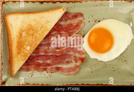 Close up petit-déjeuner anglais, côté ensoleillé d'oeufs, la moitié de pain grillé et les tranches de bacon grillé sur plaque bleue, augmentation de la vue supérieure, juste au-dessus Banque D'Images