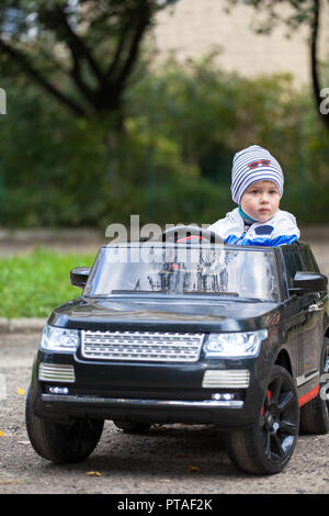 Cute boy dans une voiture électrique noir dans le parc. Funny boy montè sur un jouet voiture électrique Banque D'Images