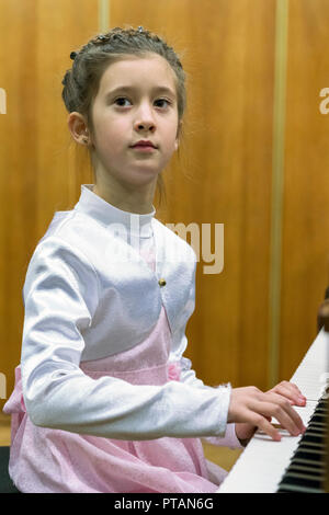 Jeune fille jouant du piano. Une fille dans une belle robe joue sur un piano à queue marron photo verticale. Banque D'Images