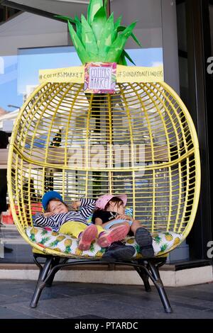 Des enfants assis et se prélasser dans un grand fauteuil d'ananas, goupilles marché sur Flinders Street, Central Business District de la ville de Townsville QLD, Australie Banque D'Images