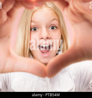 Beautiful smiling girl prend la forme d'un cœur avec ses mains sur le fond rose. Geste d'amour par de jolies jeunes enfant. Banque D'Images