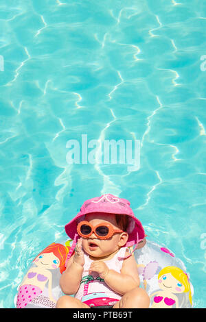 Beautiful Baby Girl Wearing Hat and Sunglasses sur un flotteur dans l'eau claire Banque D'Images