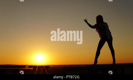 Jeune fille en uniforme de sport se trouve sur le bord du toit pendant le coucher du soleil Banque D'Images