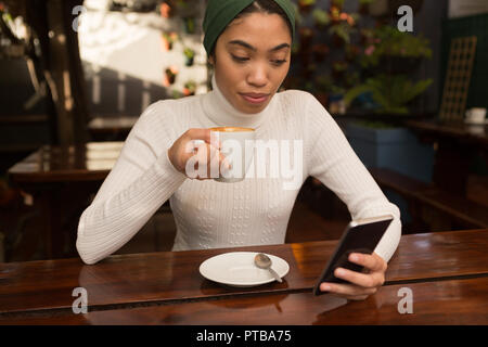 Woman using mobile phone while having coffee in cafe Banque D'Images