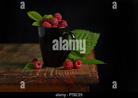 Framboises fraîches dans une tasse sur une surface en bois. Banque D'Images