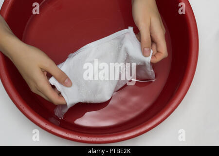 La jeune fille efface un T-shirt blanc dans un bassin rouge de stains, nettoie de stain remover, close-up, les mains, fond blanc Banque D'Images