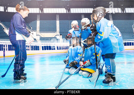 Vue de côté portrait de jeunes garçons et filles, les joueurs de hockey sur glace, à l'écoute de entraîneuse au cours de session de formation Banque D'Images