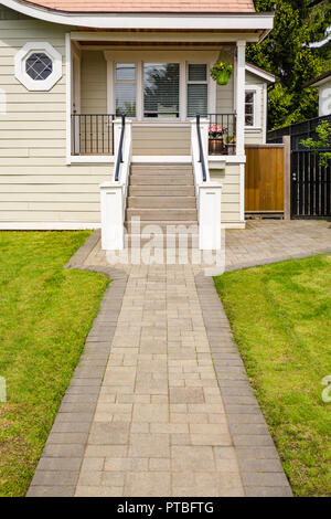 Entrée principale de la petite maison d'habitation avec allée pavée sur pelouse verte de la cour avant. Maison de famille avec porte à l'entrée sous le porche Banque D'Images