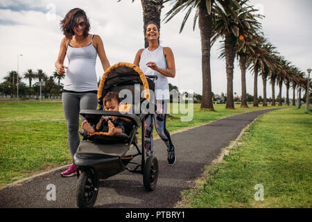 Deux Femmes Marchant Avec Un Bebe Landau Dans Un Parc Femme Enceinte Sur Une Marche Matinale Avec Son Bebe Dans Une Poussette Photo Stock Alamy