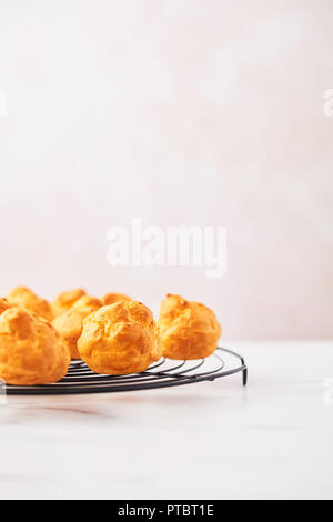 Bouquet de chou à la crème fraîche des gâteaux sur une grille française sur table en marbre blanc sur fond rose avec copie espace. Focus sélectif. Banque D'Images