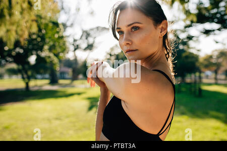 Close up of young woman l'échauffement avant une course à l'extérieur. Coureuse faisant des exercices d'étirement en matinée au parc. Banque D'Images