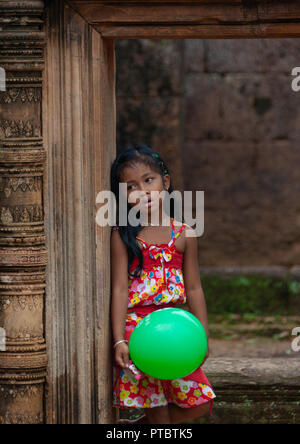Petite fille cambodgienne avec un ballon vert dans la porte de temple de Banteay Srei, la Province de Siem Reap, Angkor, Cambodge Banque D'Images