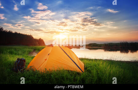 Par l'orange tente lac. Tente d'Orange se situe sur les rives de l'herbe verte au coucher du soleil. Le concept de la vie privée et les voyages. Banque D'Images