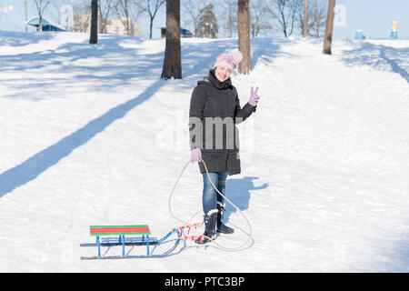 Une femme dans un manteau d'hiver noir avec traîneaux dans un parc couvert de neige ou la forêt. Banque D'Images