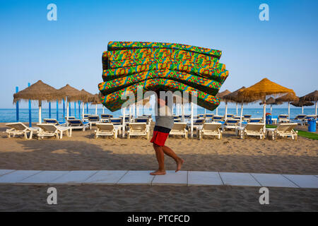 Fuengirola, Espagne - 23 juin 2018: Un ouvrier enlève des coussins de chaise de salon colorés pour la nuit alors que le soir tombe sur la plage de Coata del sol. Banque D'Images