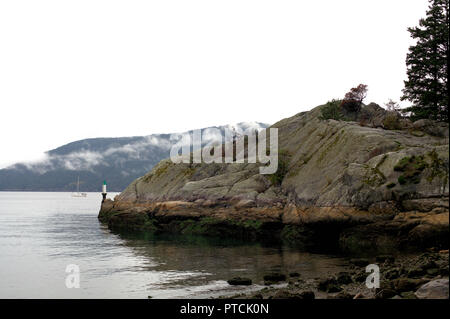 La côte rocheuse de Whytecliff Park, dans l'ouest de Vancouver, BC, Canada, sur un jour nuageux et pluvieux, montrant la mer et un voilier dans l'arrière-plan Banque D'Images