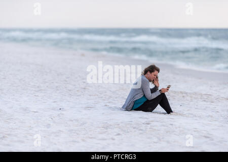 Santa Rosa Beach, USA - 24 Avril 2018 : une femme assise sur le sable blanc en Floride, petite ville à l'autre dans le golfe du Mexique de l'océan avec poile dur vagues Banque D'Images