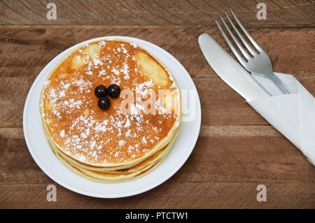 Les crêpes sur une plaque blanche sur des planches de bois avec une cuillère et fourchette enveloppée dans une serviette Banque D'Images