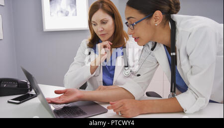 Jeune latine doctor looking at laptop computer et parler avec frère médecin Banque D'Images