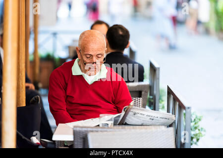 Rome, Italie - le 4 septembre 2018 : Closeup portrait of elderly senior homme chandail rouge en italien reading newspaper in street cafe dans centre historique de la ville de mo Banque D'Images