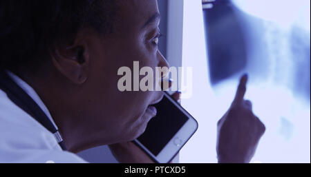 Milieu de MD noir talking on mobile phone avec le patient à propos de x ray Banque D'Images