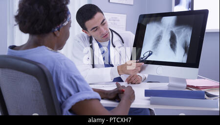 Femme noire à l'écoute de jeune MD comme il examine son x-ray Banque D'Images