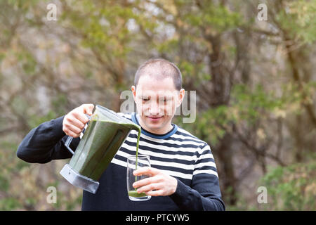 Jeune homme debout à l'extérieur, en plein air, holding plastic contenant du mélangeur, verre, verser le smoothie vert fabriqué à partir de légumes verts, Banque D'Images