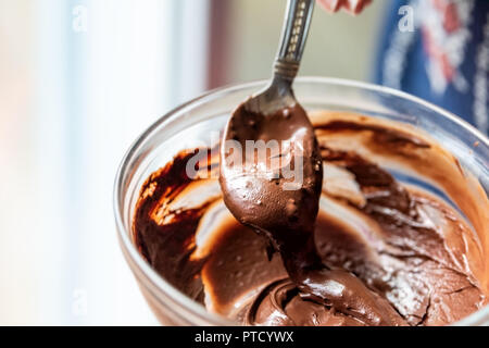 Gros plan du hand holding spoon, en remuant le mélange liquide végétalien premières, crémeux de la mousse au chocolat, la crème, le sucre à glacer dans un bol, plaque, lave Banque D'Images