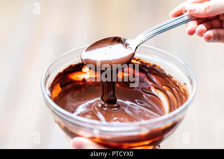 Closeup of woman hand holding spoon, mixage, fluide, en remuant végétalien premières liquide, crémeux, doux mousse au chocolat, crème glacée, le givrage dans bol, plaque, lave Banque D'Images