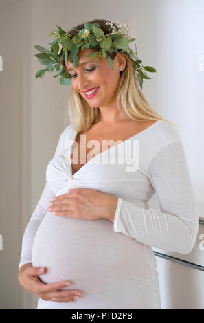 Femme, mariée, avec guirlande de fleurs, enceinte de neuf mois, holding pregnat ventre avec ses mains, Allemagne Banque D'Images