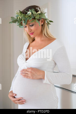 Femme, mariée, avec guirlande de fleurs, enceinte de neuf mois, holding pregnat ventre avec ses mains, Allemagne Banque D'Images