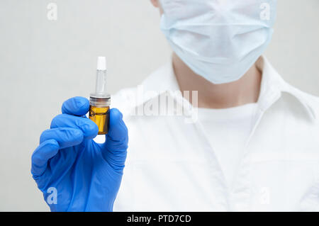 Médecin cosmetician masque en conserve dans sa main en bleu gants ampoule de médicament sur fond blanc close-up Banque D'Images