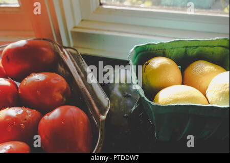 Citrons biologiques et les tomates Roma de la farmers market se dorant dans la lumière naturelle du comptoir de cuisine en marbre sur appui de fenêtre dans la cuisine gastronomique Banque D'Images