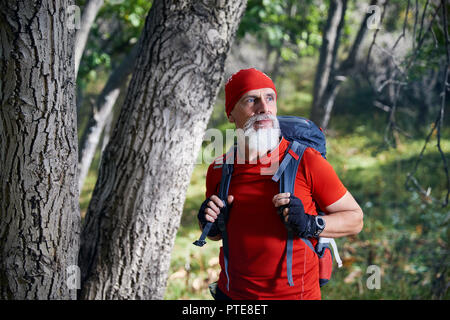 Portrait de vieil homme à barbe blanche en chemise rouge et son sac à dos dans la forêt Banque D'Images