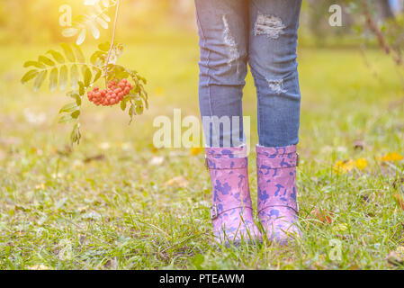 Les pieds des enfants dans des bottes en caoutchouc sur l'herbe jaunie en automne Banque D'Images