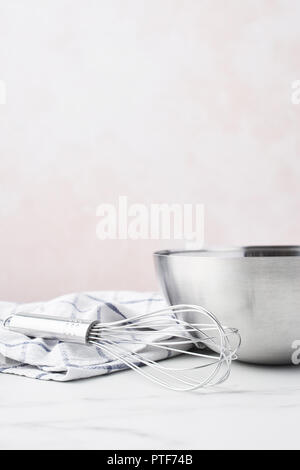 Concept de cuisson. Bol avec un fouet et table en marbre blanc sur torchon sur fond rose avec copie espace. Banque D'Images