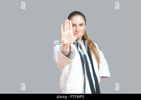 Jeune femme sportive agressive en kimono blanc avec ceinture noir s'enroule autour du cou et de l'arrêt permanent vous. Karaté japonais et sports concept. en Banque D'Images