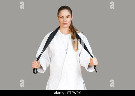 Confiant femme athlétique attrayant en kimono blanc debout et s'enroule autour du cou de ceinture noire, en regardant la caméra. Karaté japonais et des sports d'hiver Banque D'Images
