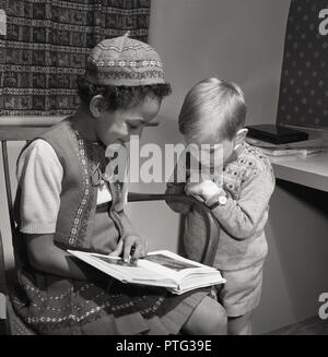 1958, historiques, jeune fille assis à l'intérieur sur une chaise avec un livre d'images, montrant les pages d'un petit garçon, England, UK. Banque D'Images