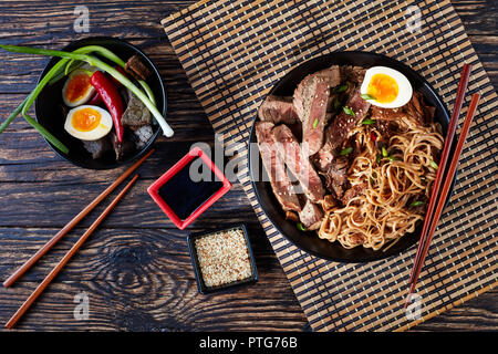 Un bol de Soba avec des tranches de rôti de bœuf, champignons shiitake, la moitié d'oeuf dur et les légumes avec des baguettes de bambou sur un tapis de table. Ingrédients sur une r Banque D'Images