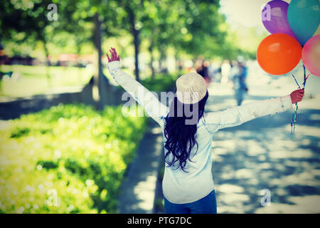 Composite image vue arrière de carefree woman holding colorful balloons Banque D'Images