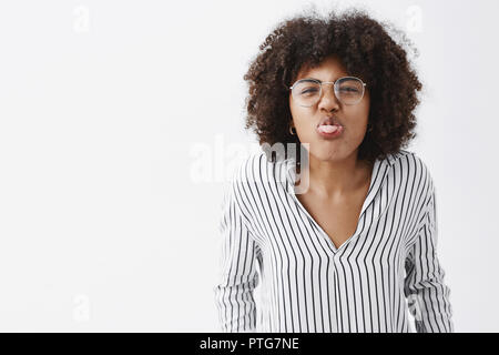 Jusqu'à la taille de balle drôle et ludique enfantin African American man avec afro hairstyle dans bureau rayé chemisier et verres massifs vers la caméra et montrant la langue nez rides joyeusement Banque D'Images