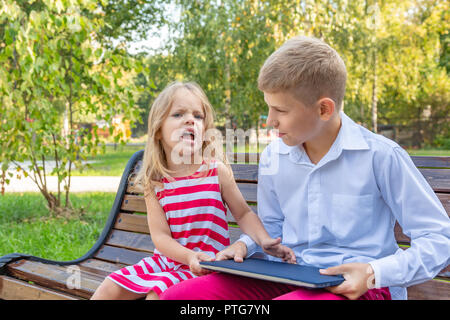 Frère et soeur dans le parc sur un banc à emporter un ordinateur portable de l'autre Banque D'Images