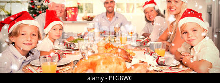 Image composite de happy family wearing santa hats autour de la table de dîner Banque D'Images