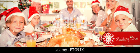 Image composite de happy family wearing santa hats autour de la table de dîner Banque D'Images