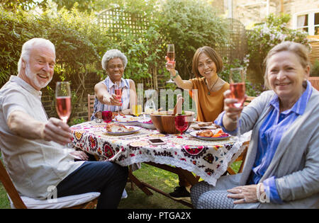 Portrait souriant, confiant senior friends drinking vin rose et profiter de déjeuner à table patio Banque D'Images