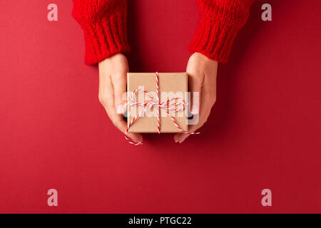 Dans les mains des femmes pull rouge avec un cadeau fort sur fond rouge. Noël et Nouvel An concept. Banque D'Images