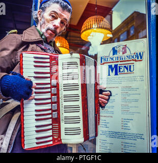 Manchester, Angleterre, RU Janvier 1989 : Un vieux musicien de rue sans-abri pose à l'extérieur d'un restaurant avec son accordéon. Prises sur des films de format moyen tran Banque D'Images