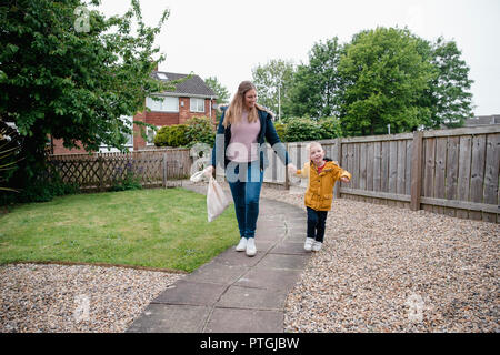 Little Boy holding sa mère part comme ils marchent le long du chemin de jardin de revenir à la Chambre. Ils sont sourire et rire sur le chemin du retour. Banque D'Images