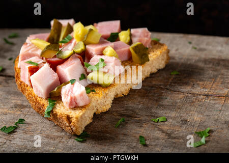 Sandwich ouvert avec des morceaux de lard fumé, de cornichons et de persil haché sur fond de bois Banque D'Images